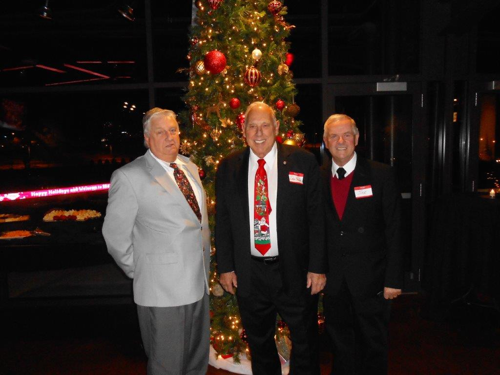 Three men in suits and ties standing next to a christmas tree.