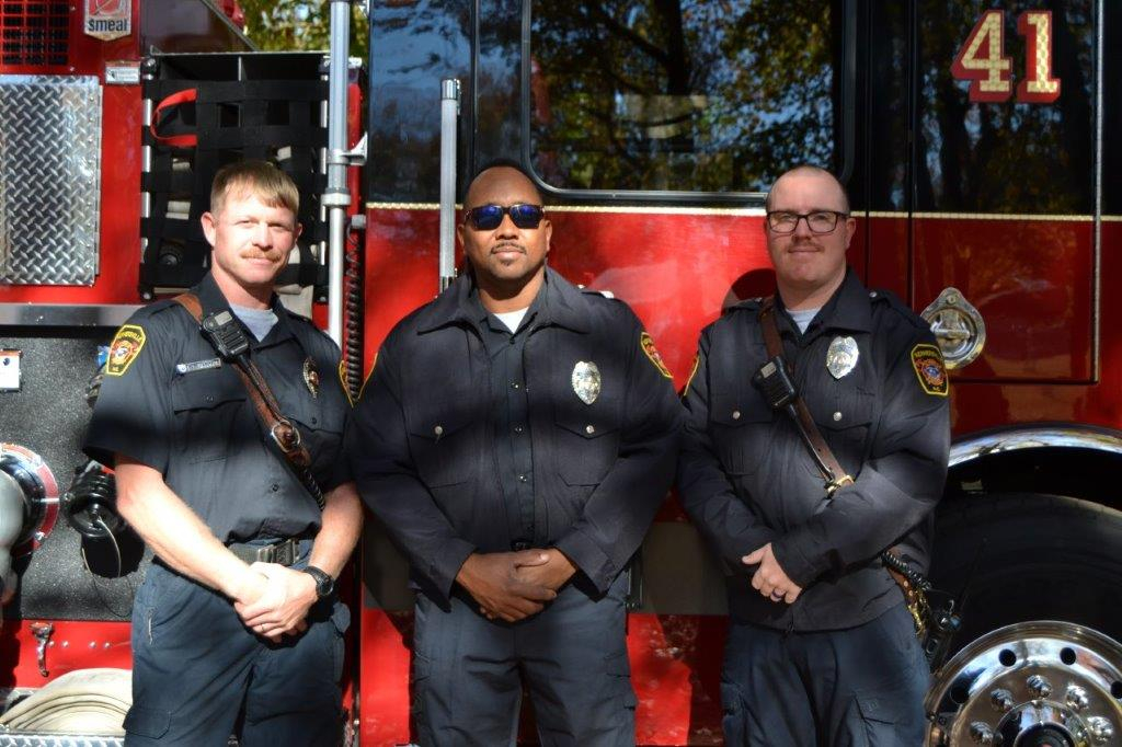 Three police officers standing in front of a fire truck.