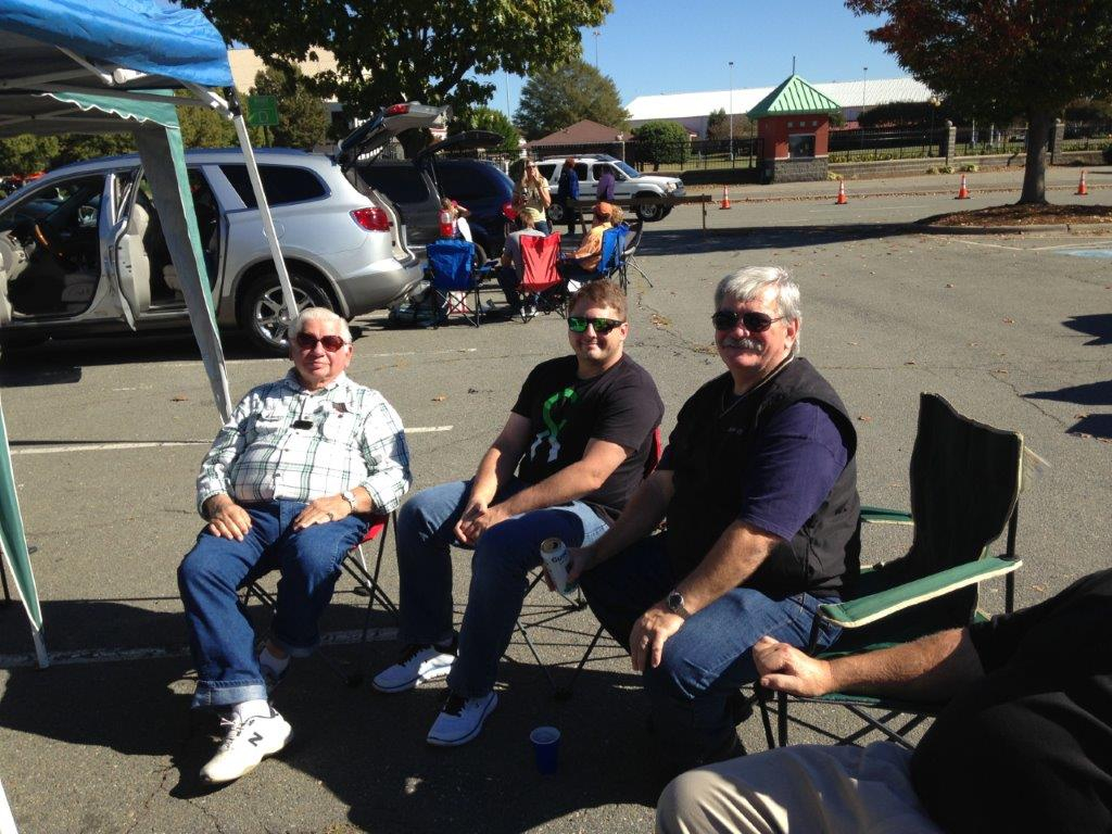 Three men sitting in lawn chairs on a street.